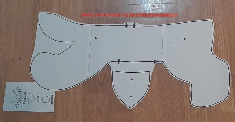 May include: A white paper craft pattern, printed on standard letter paper and assembled, with black outlines. The pattern includes shapes for a nose, tongue, and eyelashes. The text "PRINTED ON STANDARD LETTER PAPER AND ASSEMBLED" is visible.