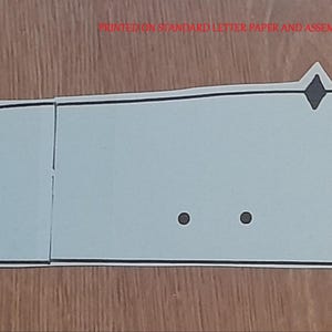 May include: A light blue, paper-based template with a black outline. The template is segmented into three rectangular sections and one curved section. Two small black dots and a diamond shape are visible.