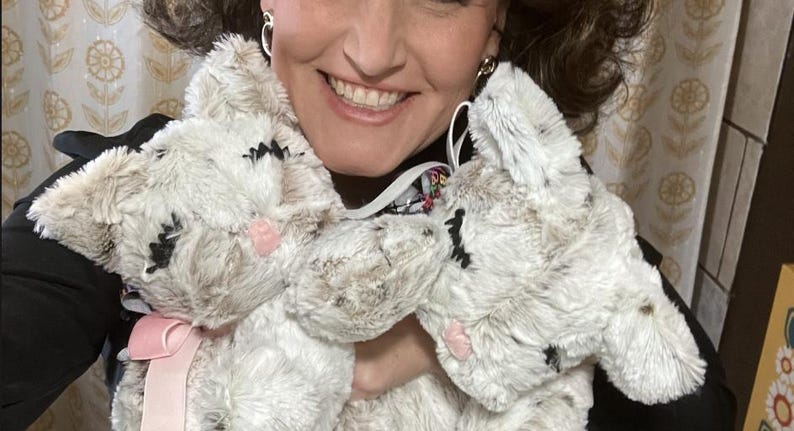 May include: Two plush bunny rabbit toys. The rabbits are white with brown accents, black embroidered eyes, and pink noses. One bunny has a pink ribbon. The toys are soft and fluffy.