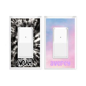 May include: Two light switch covers. One features a black and white tie-dye design with the name "NOAH" in a bold font. The other has a pastel pink and blue watercolor background with the name "averey" in a light purple font.