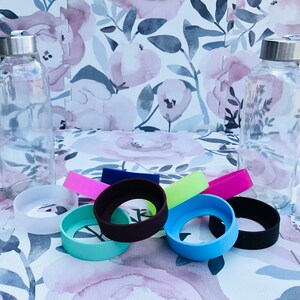 May include: Two clear glass bottles with silver lids and a variety of colorful silicone bottle koozies. The koozies are in various colors, including black, blue, green, pink, and yellow.