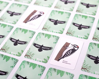 May include: A set of bird matching game cards with green foliage and a silhouette of a bird on the front. One card features a colorful illustration of a Downy Woodpecker.