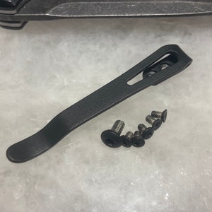 May include: A black metal pocket clip with a curved design. The clip is shown with six silver screws.