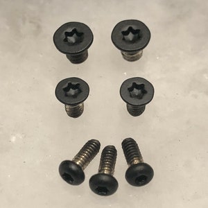 May include: A set of seven black screws, four with a star-shaped head and three with a hexagonal head.