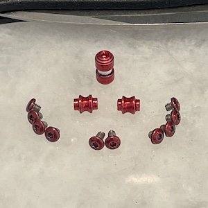 Peut inclure: Un ensemble de quincaillerie en métal rouge pour un projet. L'ensemble comprend deux petits cylindres en métal rouge, deux petites vis en métal rouge et six petites vis en métal rouge à tête en étoile.