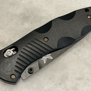 May include: Black folding knife with a textured black handle and a silver blade. The knife has a small silver button on the handle and the word "Benchmade" is engraved on the blade.