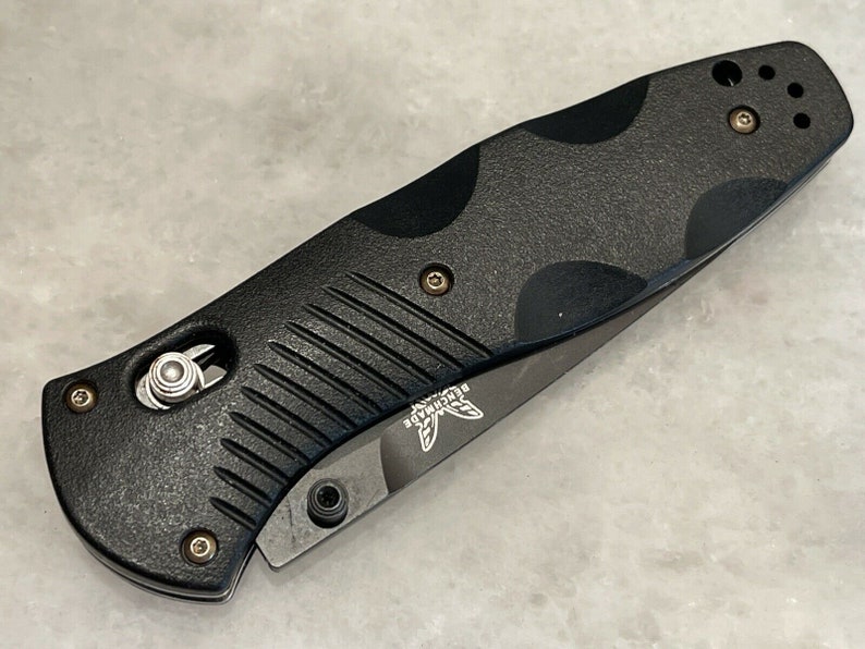 May include: Black folding knife with a textured black handle and a silver blade. The knife has a small silver button on the handle and the word "Benchmade" is engraved on the blade.