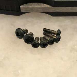 May include: Close-up of seven black screws with a star-shaped head.