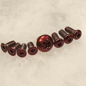 May include: A set of eight red-toned screws with a star-shaped head. The screws are arranged in a semi-circle with a larger, red-toned screw in the centre.