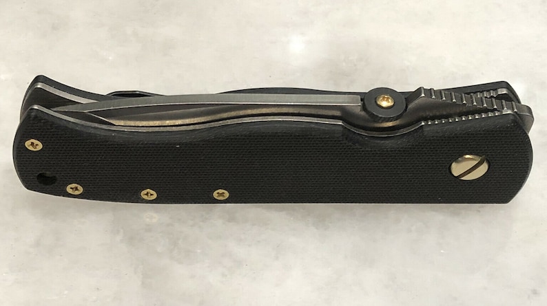 May include: A black folding knife with a textured handle and gold accents. The knife is closed and has a partial view of the blade.