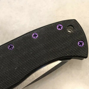 May include: Close-up of a black pocket knife with purple screws. The knife has a black handle and a silver blade.