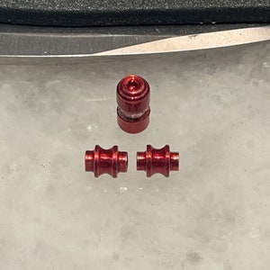 Puede incluir: Tres cuentas de metal rojo, dos son cilíndricas y una es una cuenta redonda con un centro elevado.