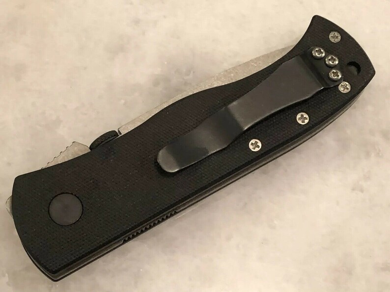 May include: Black folding knife with a black pocket clip and a textured black handle. The knife has a silver blade and a silver pocket clip.