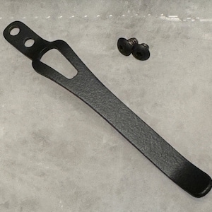 May include: Black metal pocket clip with two screws. The clip has a textured finish and a curved shape.