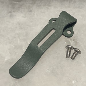 Puede incluir: Un clip de bolsillo de metal verde con dos tornillos. El clip está diseñado para sujetarse a un bolsillo o cinturón.