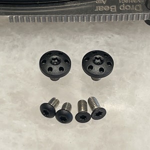 May include: Five black screws with a star-shaped head and a black plastic cap. The screws are arranged in a row on a white surface.