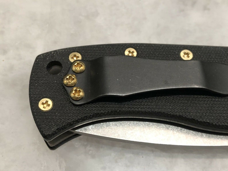 May include: A black folding knife with a textured handle and gold screws. The knife has a pocket clip.