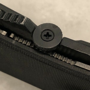 May include: Close-up of a black pocket knife with a textured handle and a silver screw.
