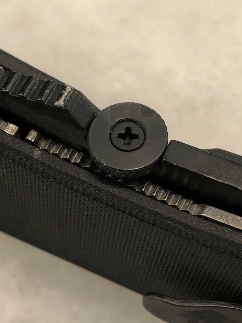 May include: Close-up of a black pocket knife with a textured handle and a silver screw.