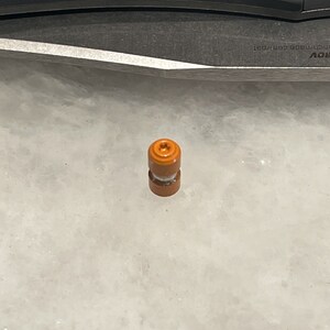 Puede incluir: Un pequeño objeto cilíndrico naranja y blanco con una parte superior con forma de tornillo.