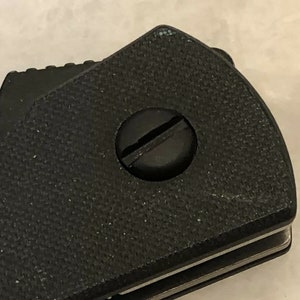 Puede incluir: Primer plano de una navaja de bolsillo negra con un mango texturizado y un tornillo plateado.
