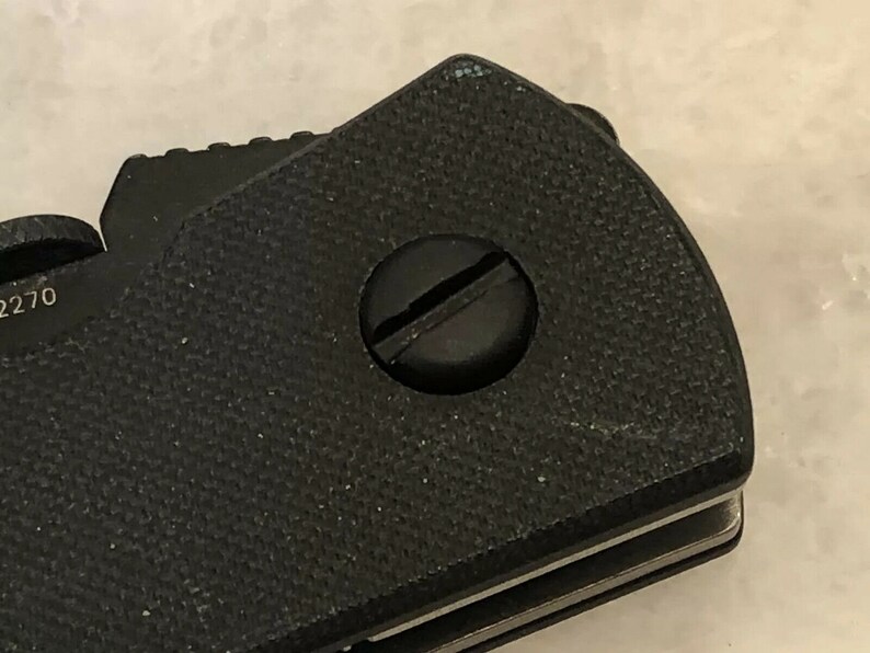 Puede incluir: Primer plano de una navaja de bolsillo negra con un mango texturizado y un tornillo plateado.