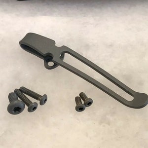 Può includere: Un fermaglio per tasca in metallo grigio con quattro piccole viti nere.