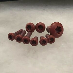 May include: A set of eight red star-shaped screws. The screws are made of metal and have a star-shaped head.