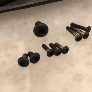 May include: A collection of eight black screws with a star-shaped head.