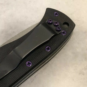 May include: A black pocket knife with purple screw detail. The knife has a black handle and a silver blade.