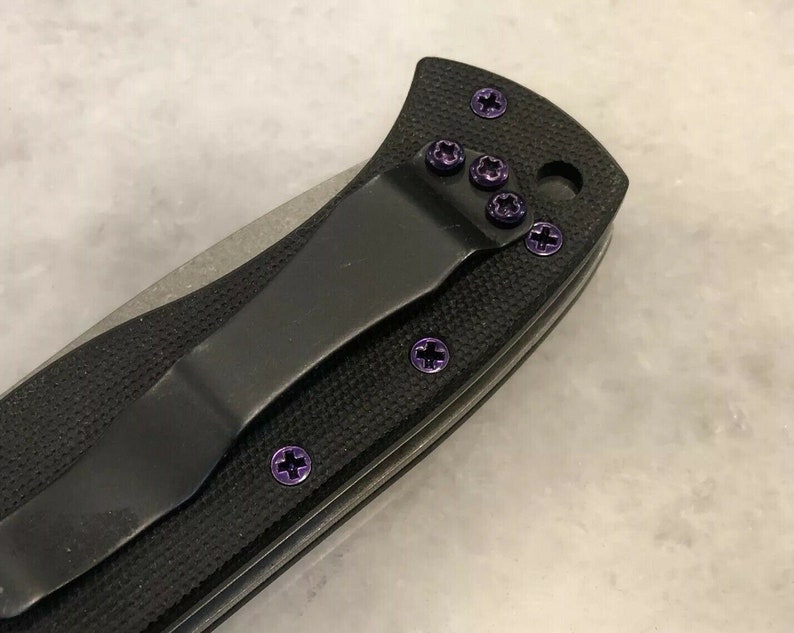 May include: A black pocket knife with purple screw detail. The knife has a black handle and a silver blade.