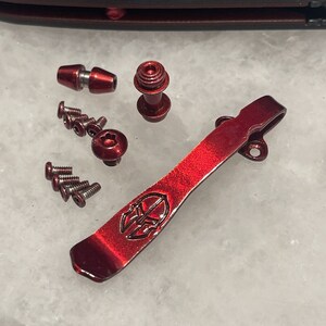 May include: A red metal pocket clip with a logo and a set of screws and other hardware.