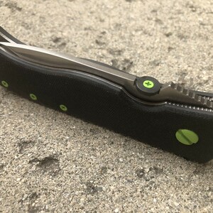 May include: A black folding knife with a partially open blade. The handle has green accents and a textured surface.