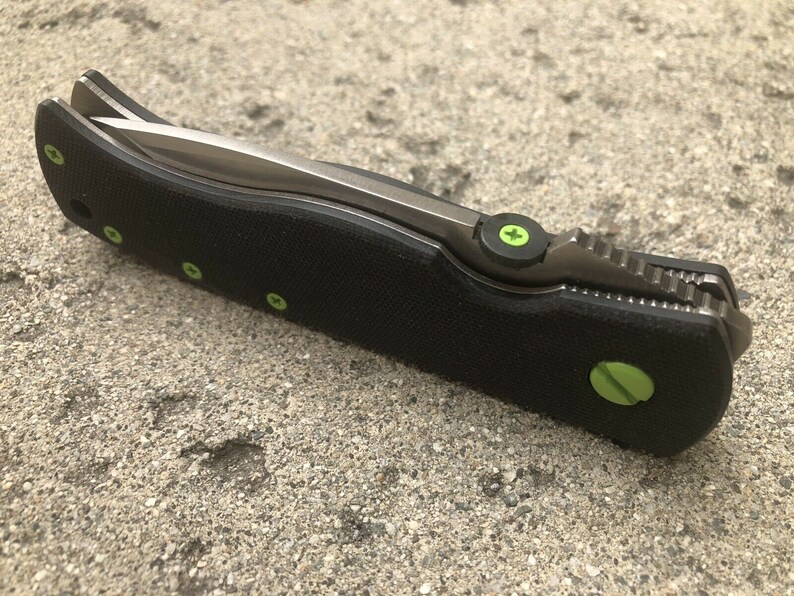 May include: A black folding knife with a partially open blade. The handle has green accents and a textured surface.