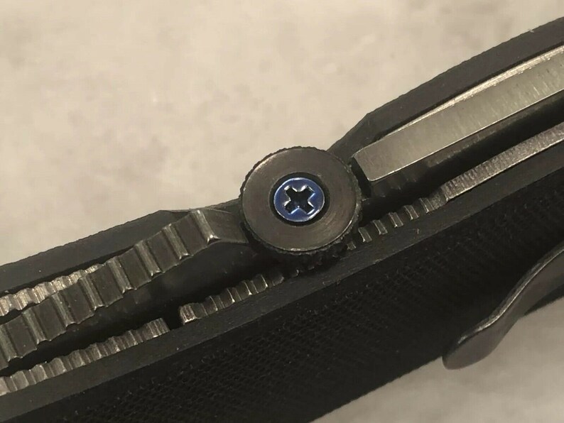 May include: Close-up of a black pocket knife with a blue screw. The screw is a Phillips head screw.