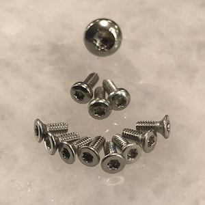 May include: An assortment of silver screws with a star-shaped recess in the head. The screws are in different sizes and shapes, including countersunk and button head types. The image is taken from a top-down perspective.