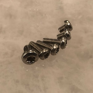 May include: A close-up of eight silver screws with a star-shaped head.