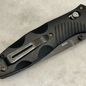 May include: Black folding knife with a textured black handle and a silver pocket clip. The knife has a black blade with the text "154CM" on it.