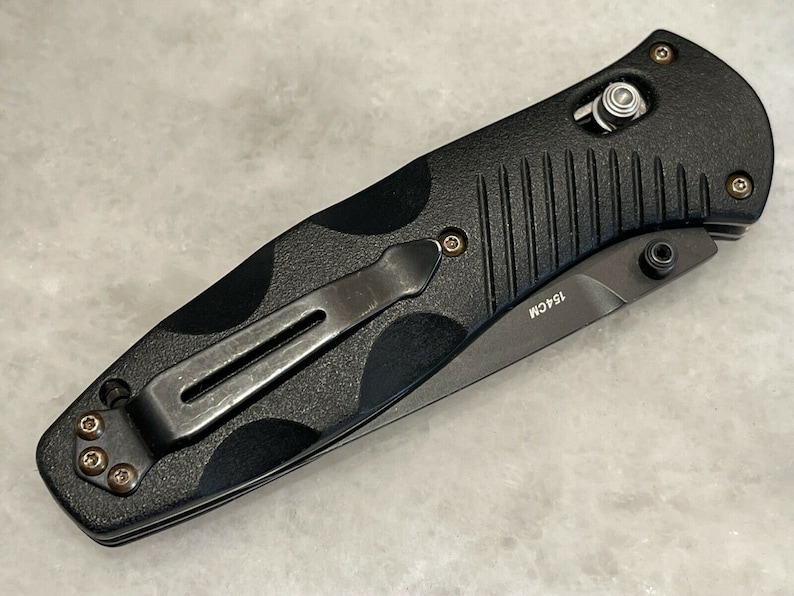 May include: Black folding knife with a textured black handle and a silver pocket clip. The knife has a black blade with the text "154CM" on it.
