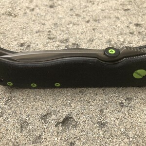 May include: A black pocket knife with a green accent on the handle and a partially open blade.