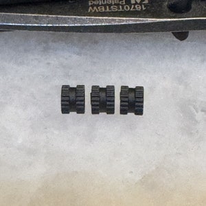 May include: Three black plastic threaded inserts, each with a hexagonal shape and a series of ridges around the circumference.