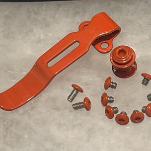 Puede incluir: Un juego de herrajes de metal naranja para una navaja de bolsillo. El juego incluye un clip de bolsillo, un botón de rosca y ocho tornillos.