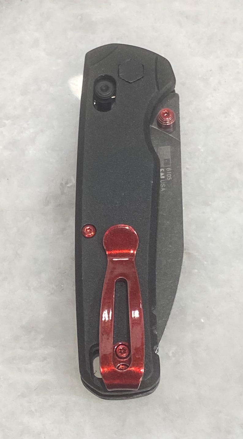 Pu&ograve; includere: Un coltello pieghevole nero con clip da tasca rossa e viti rosse. La lama &egrave; parzialmente visibile. Il coltello ha un manico strutturato e un piccolo bottone. Il coltello &egrave; contrassegnato "16105 CA USA".