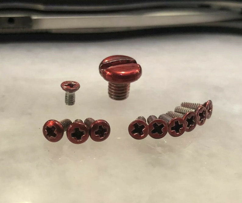 May include: A collection of red metal screws with a cross-shaped head. The screws are of various sizes, with the largest screw having a slightly rounded head.