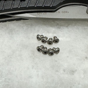May include: A close-up of ten silver screws on a white surface. The screws have a star-shaped head.