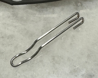 May include: A silver metal hook with a curved shape. The hook is designed to attach to a belt loop or other similar item.