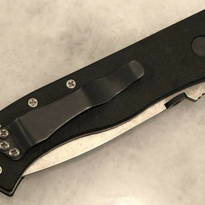 May include: A black folding knife with a black handle and a silver blade. The knife has a pocket clip and a textured handle.