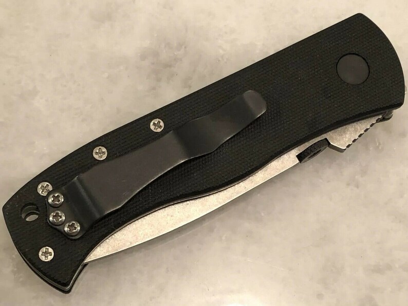 May include: A black folding knife with a black handle and a silver blade. The knife has a pocket clip and a textured handle.