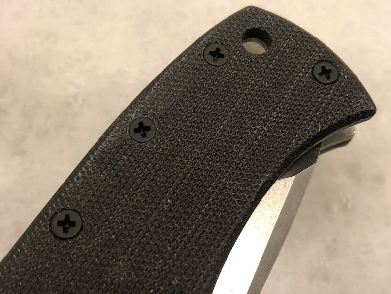 May include: Close-up of a black knife handle with a textured surface and four silver screws.