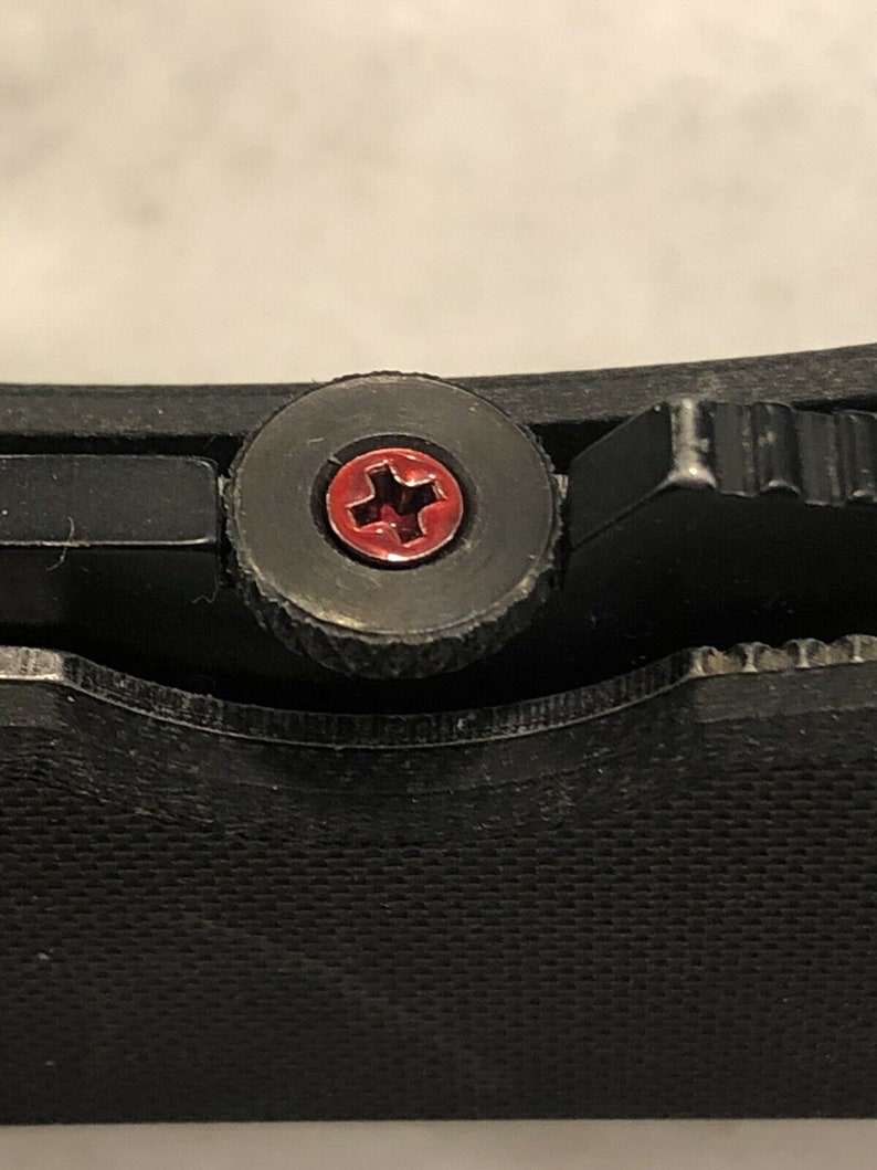 May include: Close-up of a black pocket knife with a red cross-shaped screw.